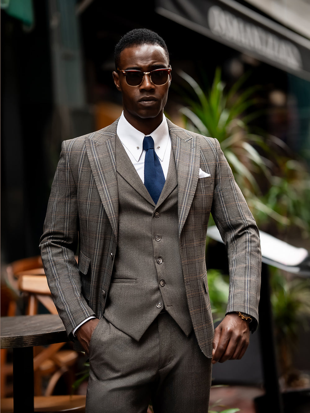 XAYWEAR brown checkered men suit with vest, white shirt, and navy tie worn by man with sunglasses