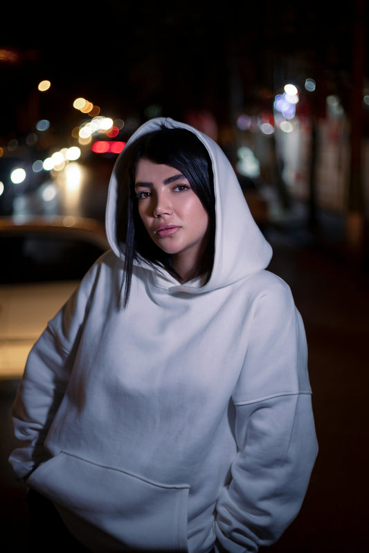 XAYWEAR white hoodie worn by woman standing on city street at night with blurred lights