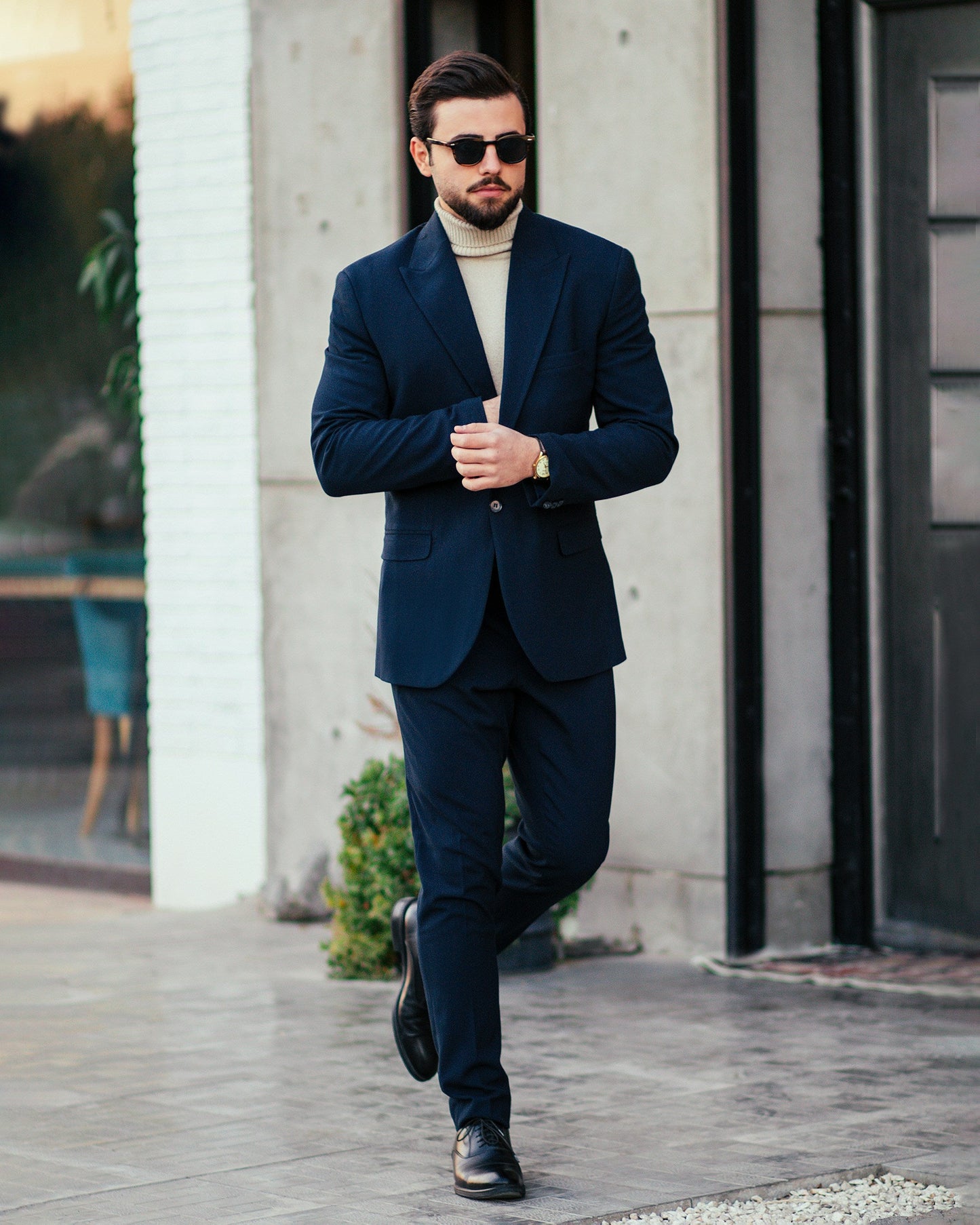 Stylish man in a navy blue suit for weddings, paired with a turtleneck and sunglasses, walking confidently