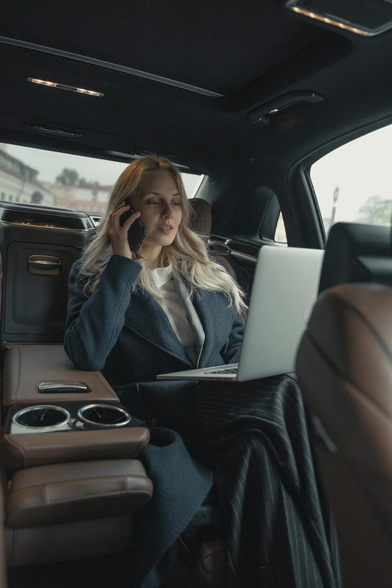 XAYWEAR stylish overcoat worn by a woman in a car while working on a laptop and talking on the phone