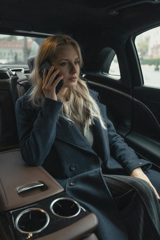 Elegant XAYWEAR overcoat in navy worn by a woman sitting in a luxury car making a phone call