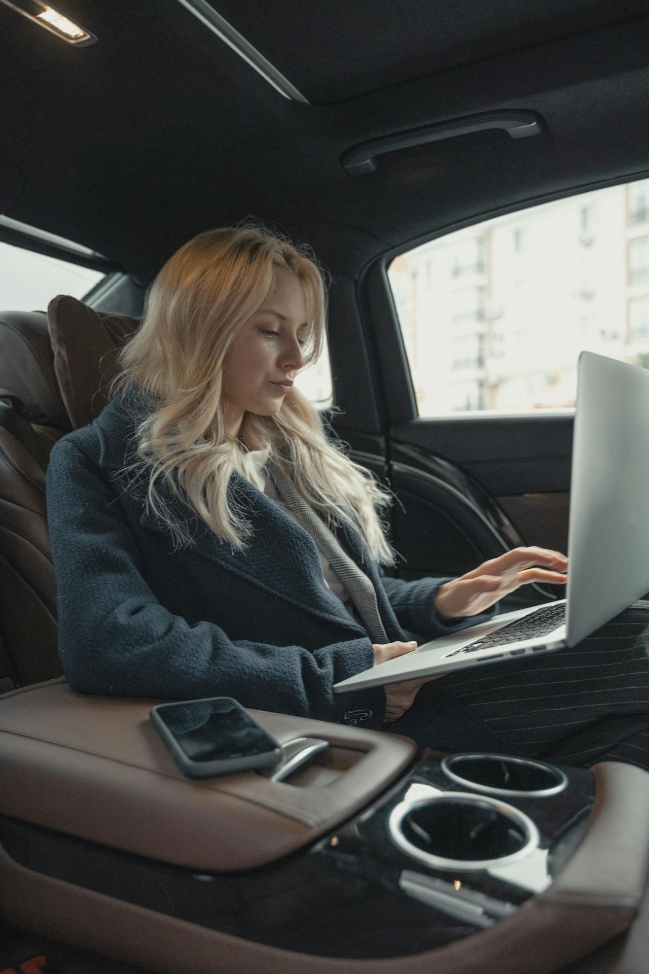 XAYWEAR stylish overcoat worn by a woman working on a laptop in a luxury car interior