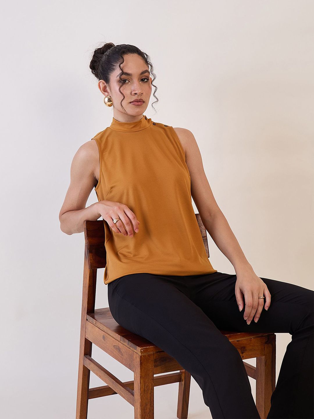 XAYWEAR high neck sleeveless top in mustard worn by woman sitting on wooden chair