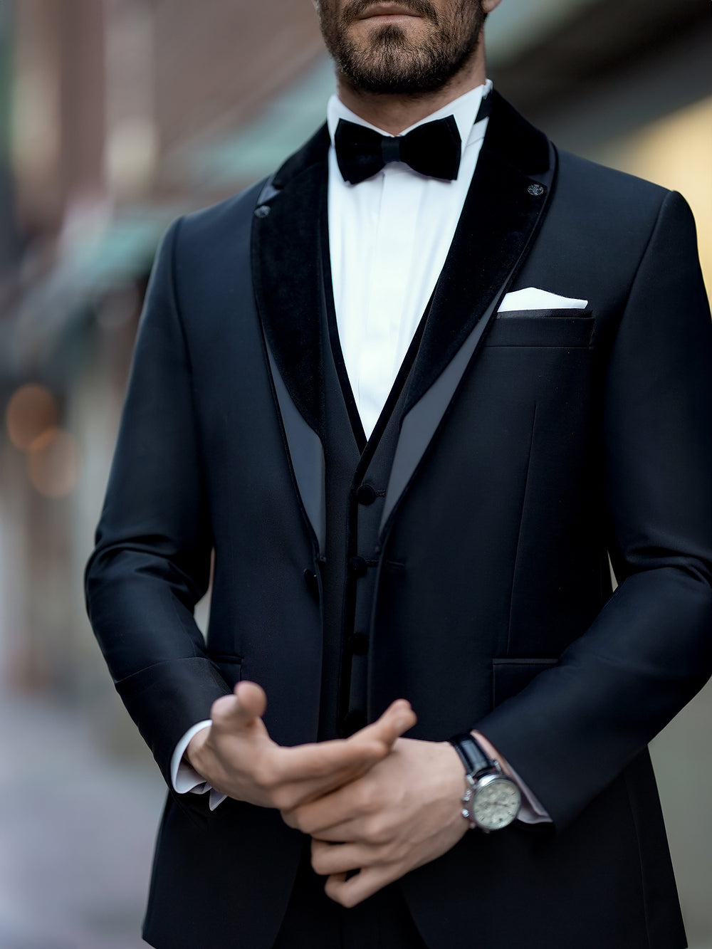 XAYWEAR black three piece suit with velvet lapels and bow tie on a man adjusting his cufflinks