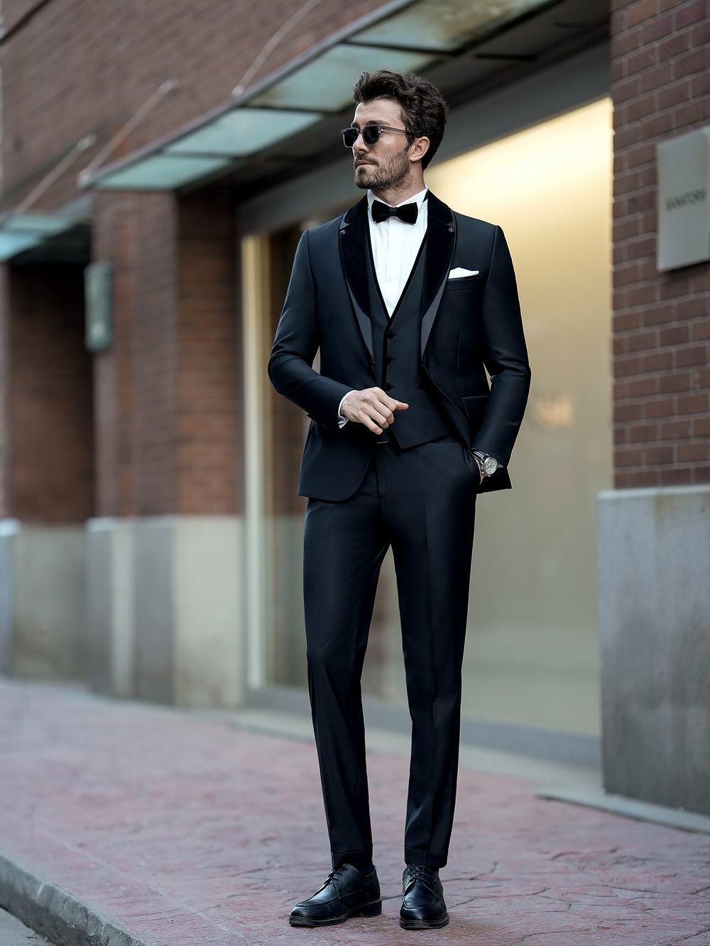 XAYWEAR black three piece suit with bow tie worn by man in sunglasses on city street