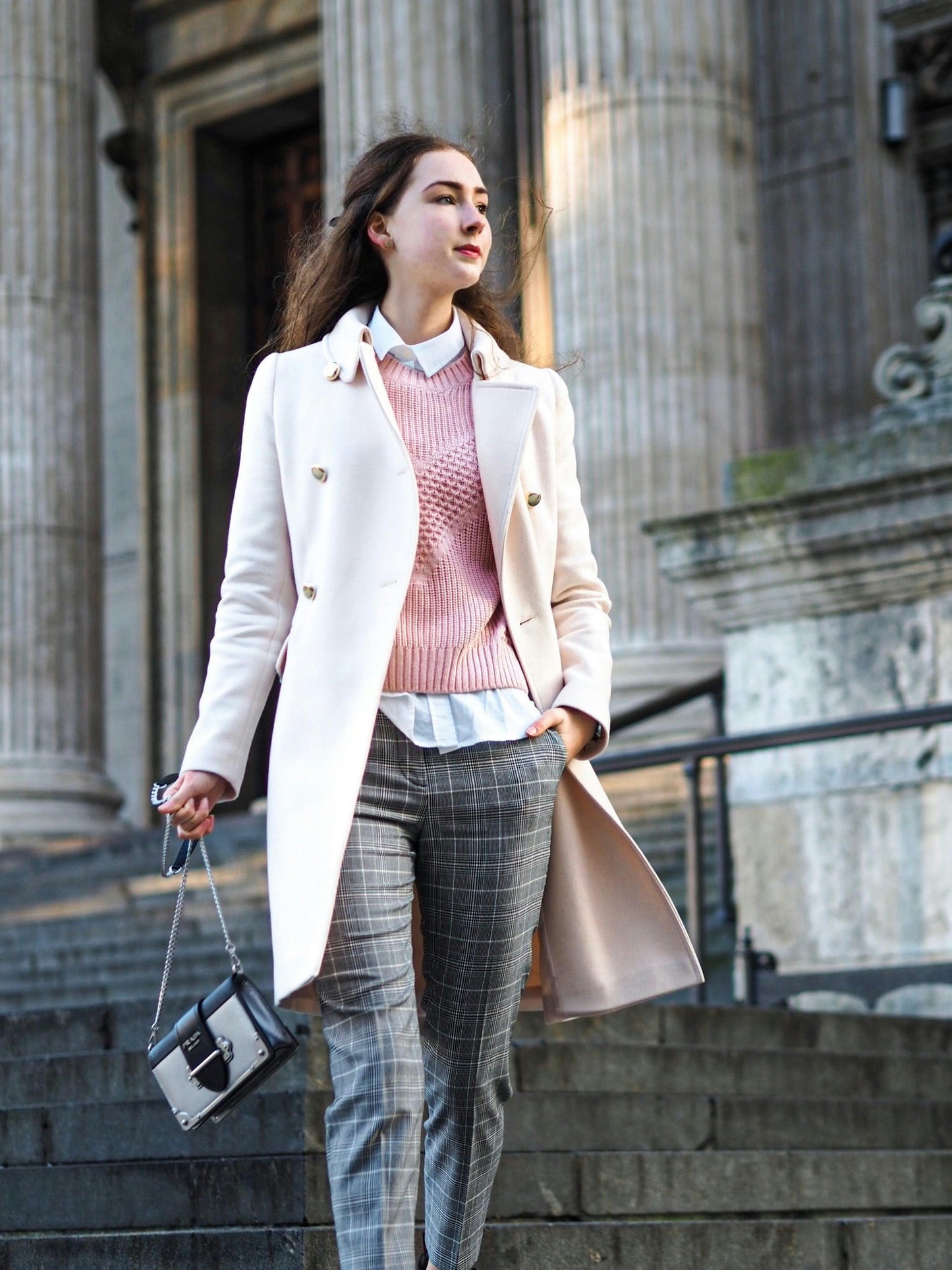 Woman wearing a light-colored trench coat for women by XAYWEAR walking down stone steps in an urban setting