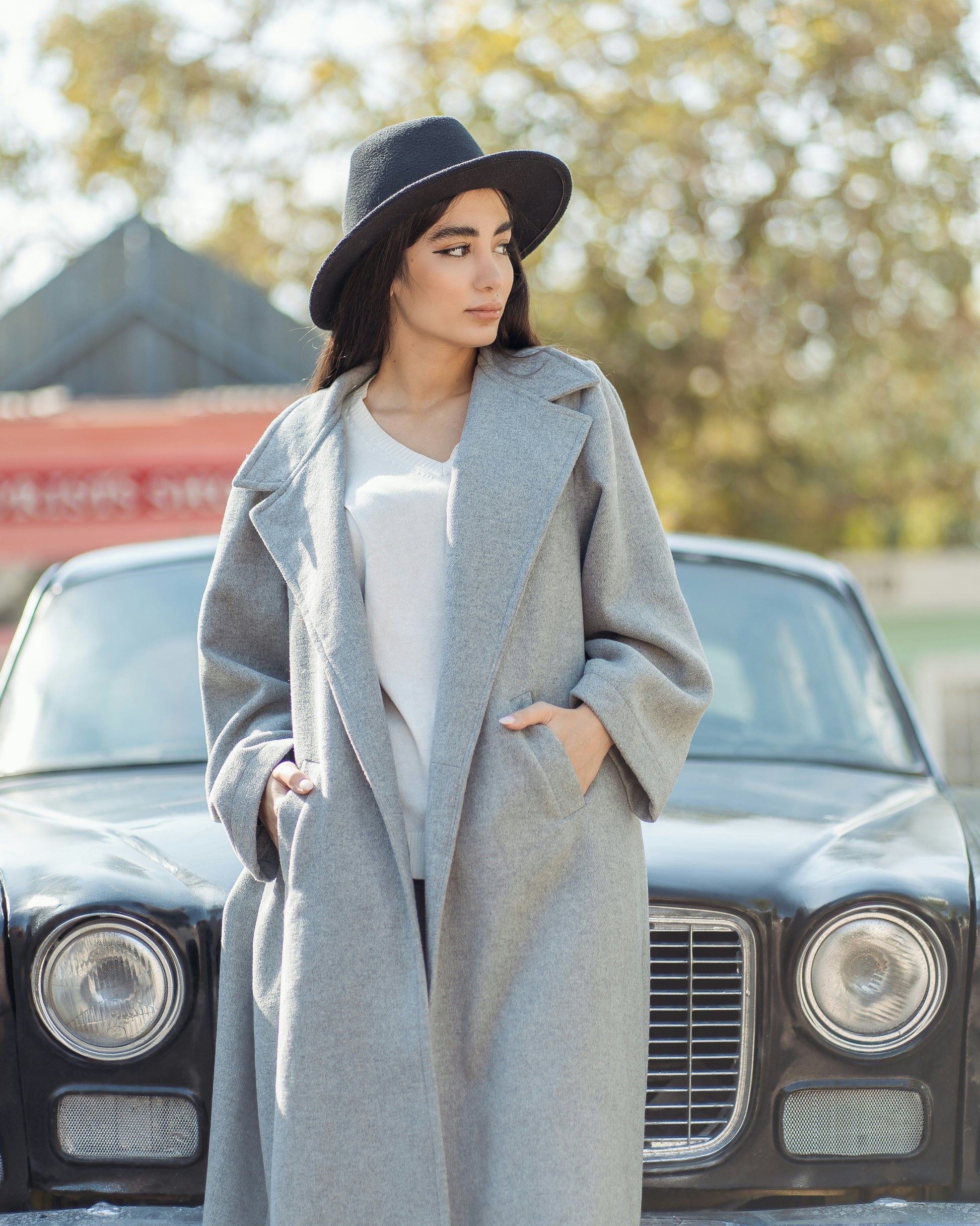 XAYWEAR trendy oversized coat for women in gray, paired with a stylish hat, standing beside a vintage car