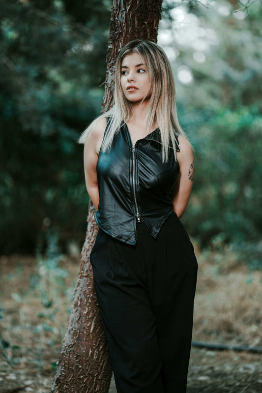 XAYWEAR black leather vest for women with front zipper worn by woman outdoors leaning on tree