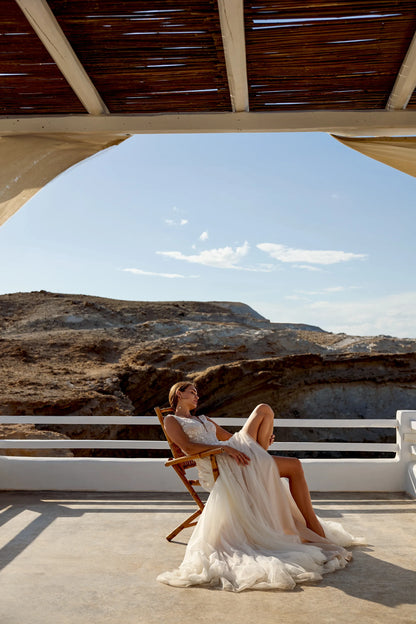 Bride wearing XAYWEAR wedding dress lounging on wooden chair with rocky landscape background