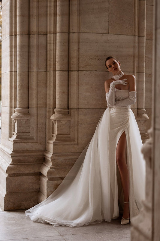Elegant XAYWEAR wedding gown with high slit and long gloves worn by model in classical stone building