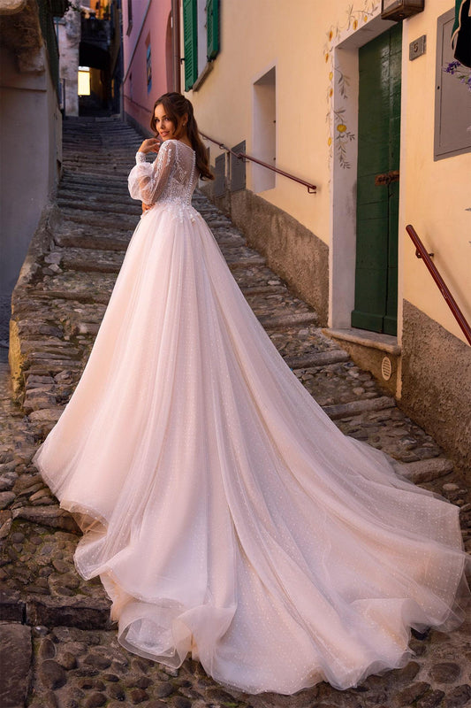 XAYWEAR white bridal gown with long train and lace sleeves on a cobblestone street