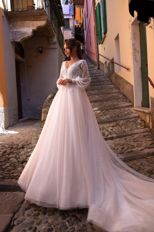 XAYWEAR white bridal gown with long sleeves and lace bodice worn on cobblestone street