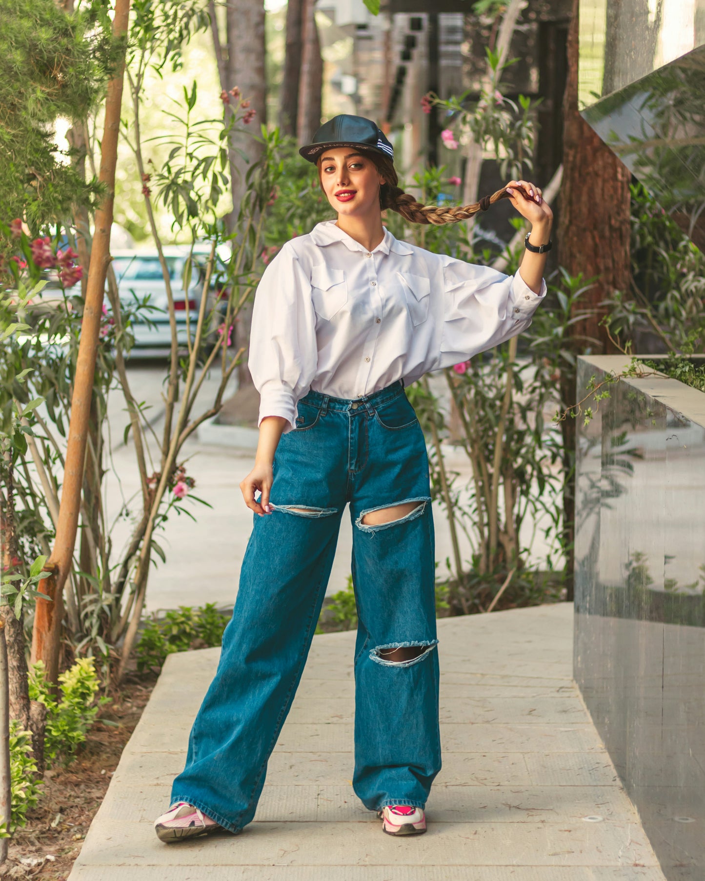 Woman wearing a white shirt for women paired with ripped blue jeans and a black cap outdoors