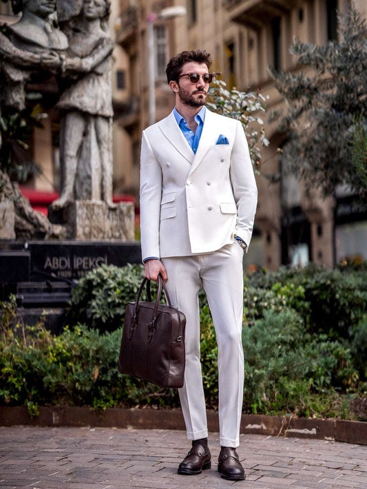 Man wearing white suit for men by XAYWEAR with blue shirt and brown leather bag in urban setting