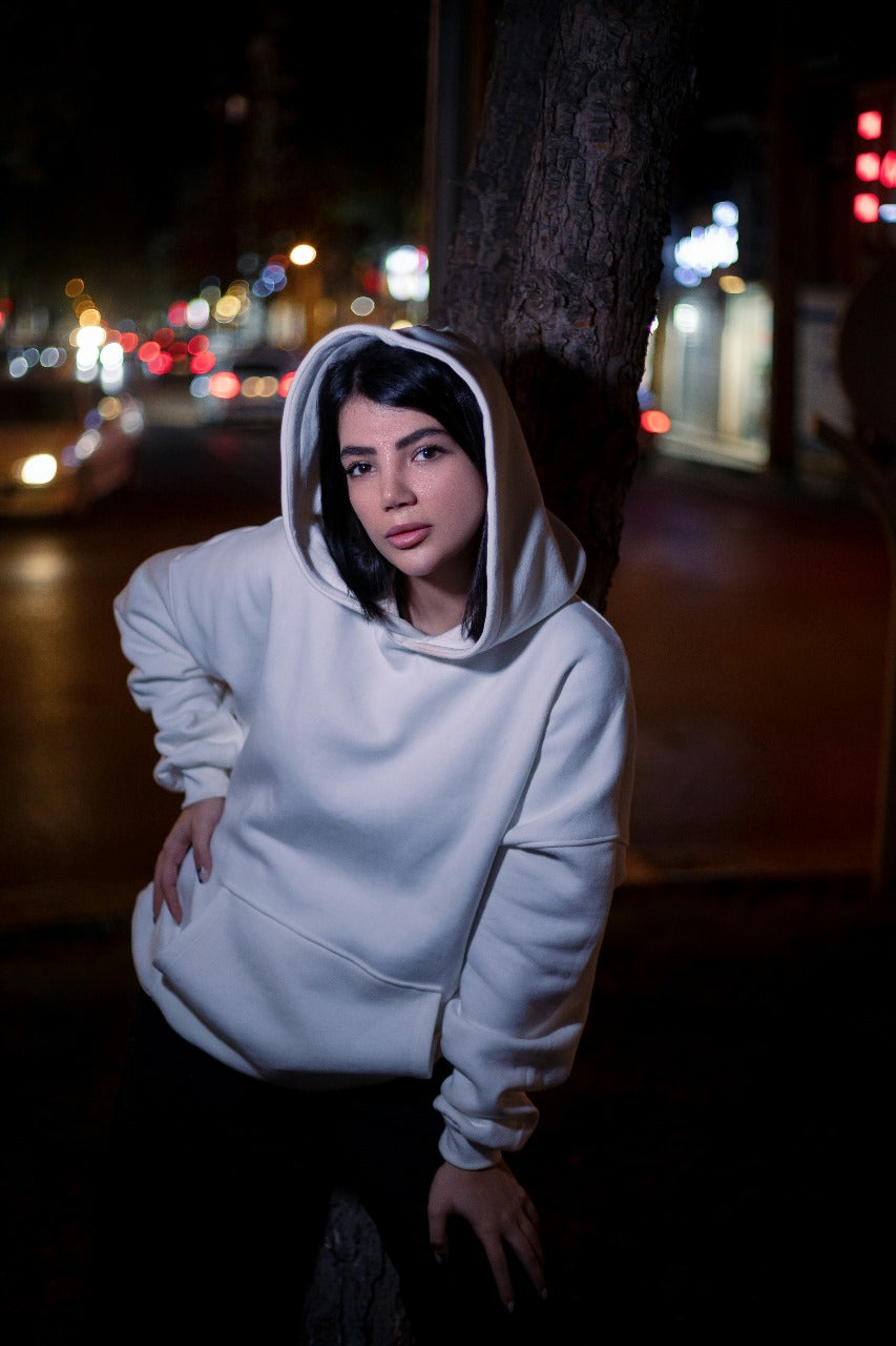 XAYWEAR white hoodie worn by woman leaning against tree with nighttime city background