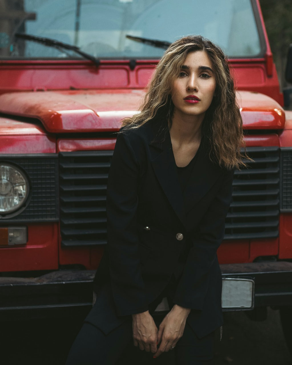 XAYWEAR women blazer in black worn by a model posing in front of a red vintage vehicle