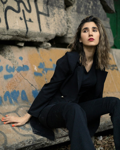 XAYWEAR women blazer in black worn by a woman sitting against a graffiti wall outdoors