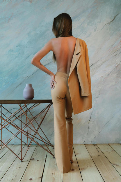 Back view of a woman wearing a beige women formal suit by XAYWEAR with blazer draped over shoulder