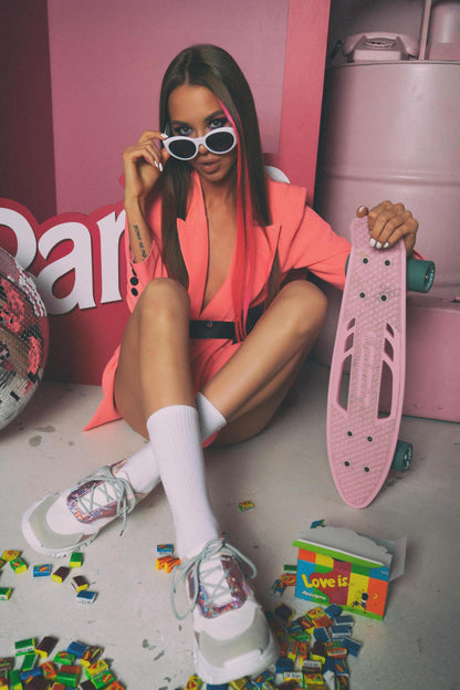 XAYWEAR women pink blazer styled with white sneakers and sunglasses holding a pink skateboard